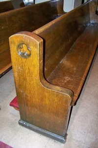 A wooden church pew with a carved symbol on the end.