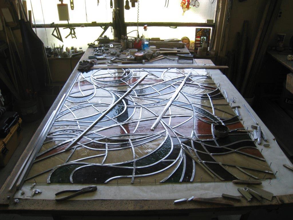Stained glass restoration project on workshop table with tools.