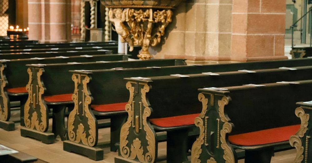Ornate wooden church pews with red cushions inside historic cathedral.