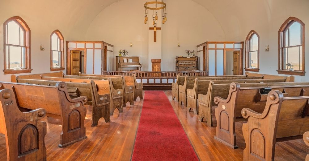 Interior of a traditional church with wooden pews, red carpet aisle, and altar with cross.