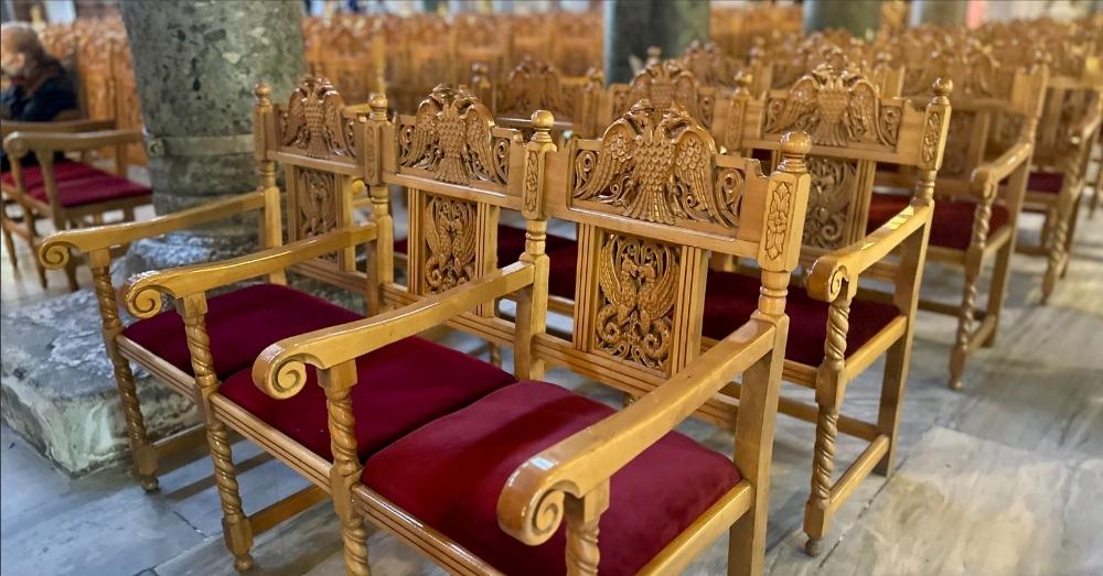 Rows of empty wooden church chairs with red velvet cushions.