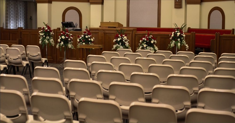 An empty church hall with chairs and floral arrangements.