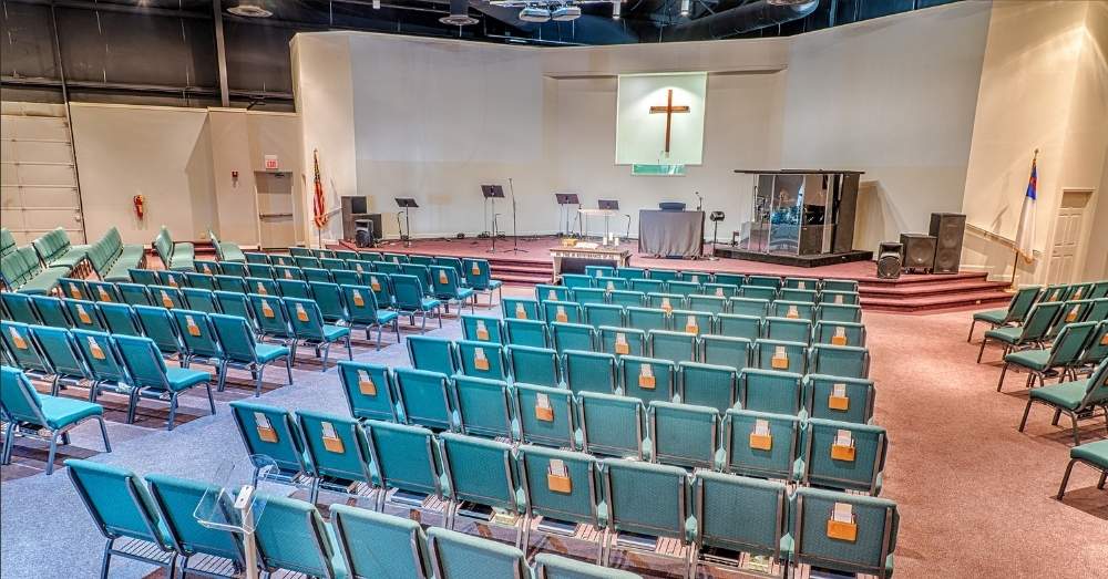 An empty church hall with rows of teal chairs.