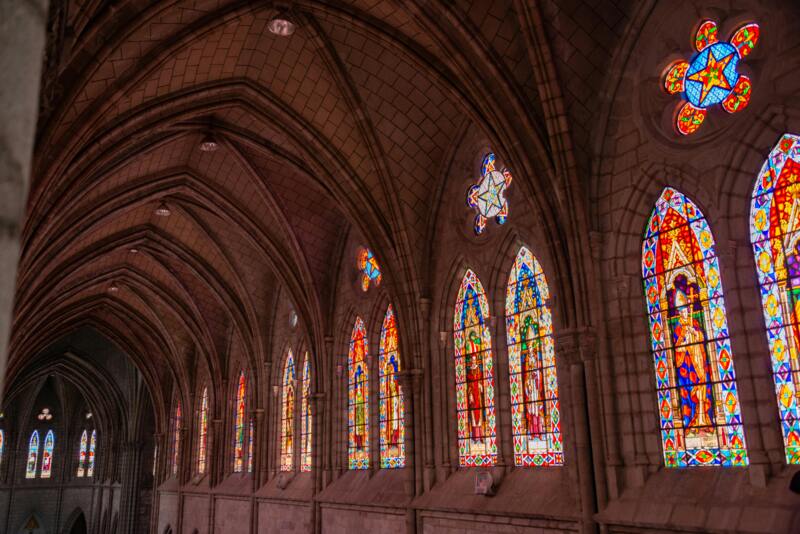 Row of tall arched stained-glass windows casting colorful light into a cathedral interior — church pew refurbishing, stained glass windows.