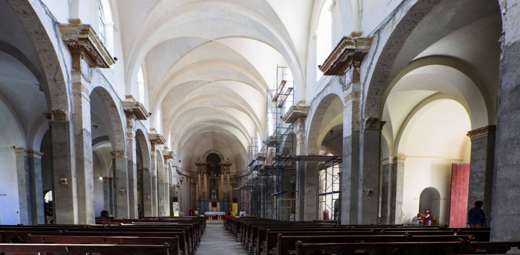 Spacious church interior with scaffolding, pillars, and pews under renovation.