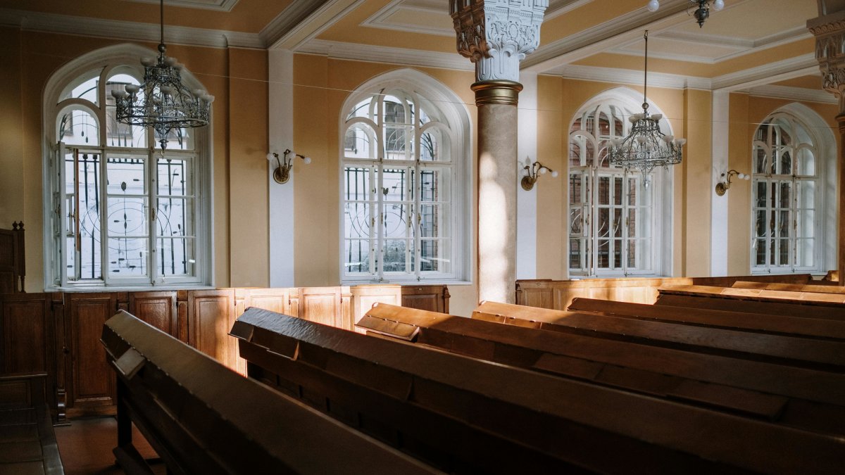 Sunlit church interior with arched windows, wooden pews, and chandeliers, representing a calm, functional sanctuary environment.