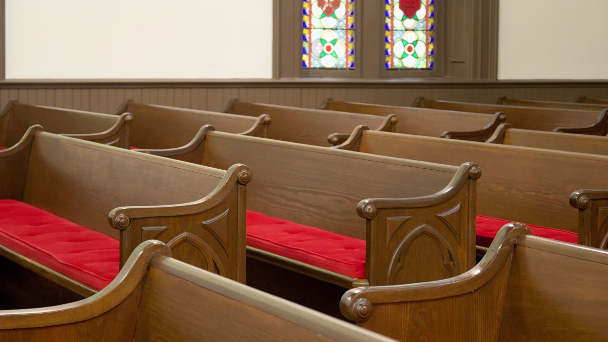 Cozy church interior with wooden pews featuring red cushions, complemented by beautiful stained glass windows.