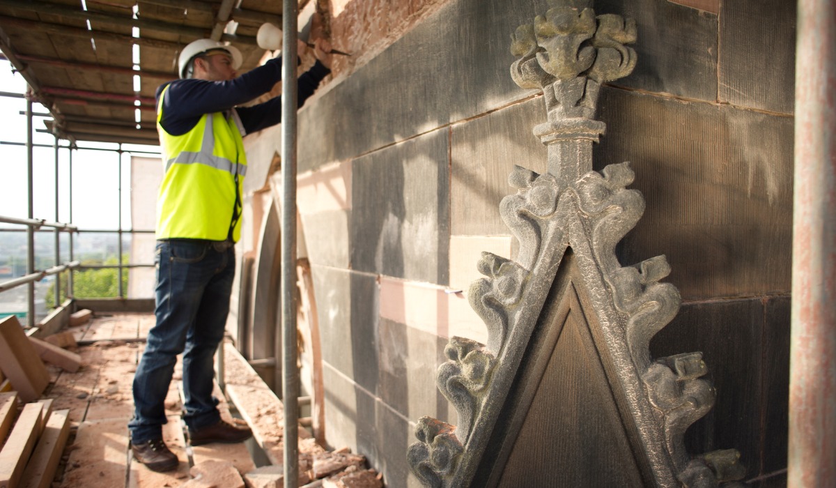 A construction worker standing on a scaffolding platform restoring ornate stone carvings